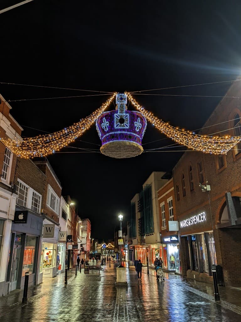 Windsor high street at night with Christmas lights and a lit crown above the wet cobbles